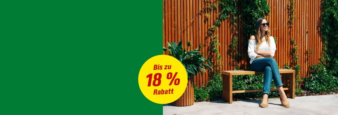 Eine Person sitzt auf einer Holzbank vor einer bewachsenen Holzwand.